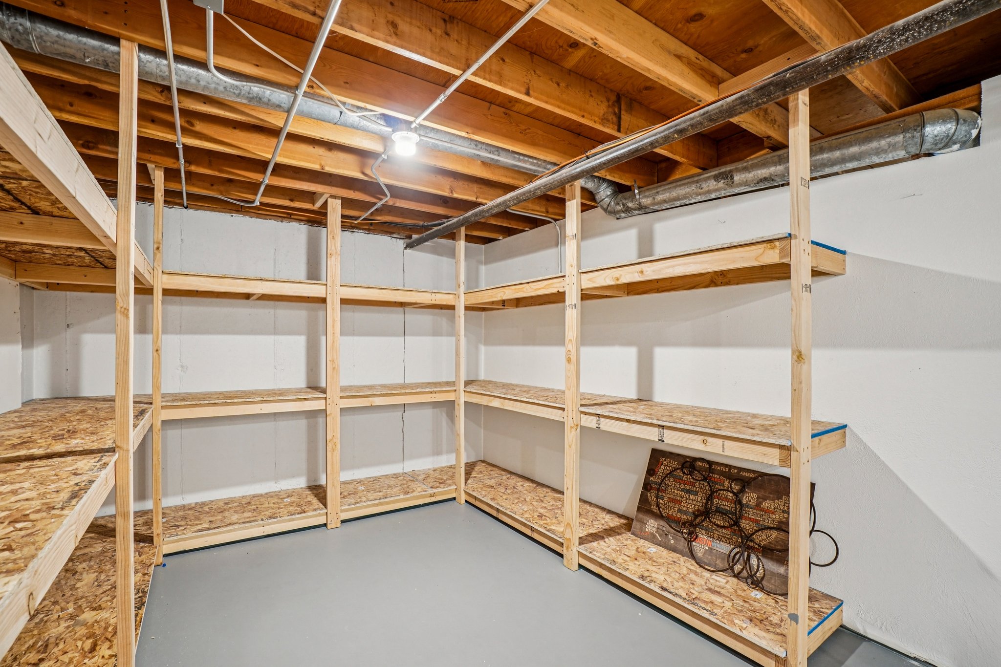 Basement storage area featuring extensive built-in shelving, painted concrete flooring, and exposed ceiling joists