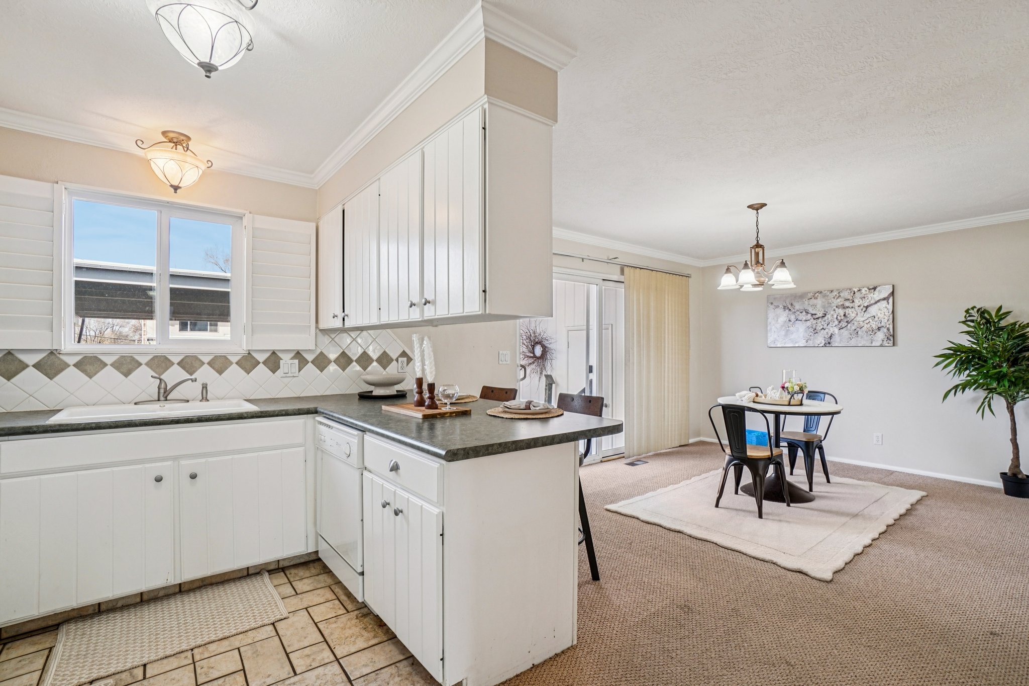 Bright kitchen featuring white cabinetry, a tiled backsplash with diamond accents, and dark countertops