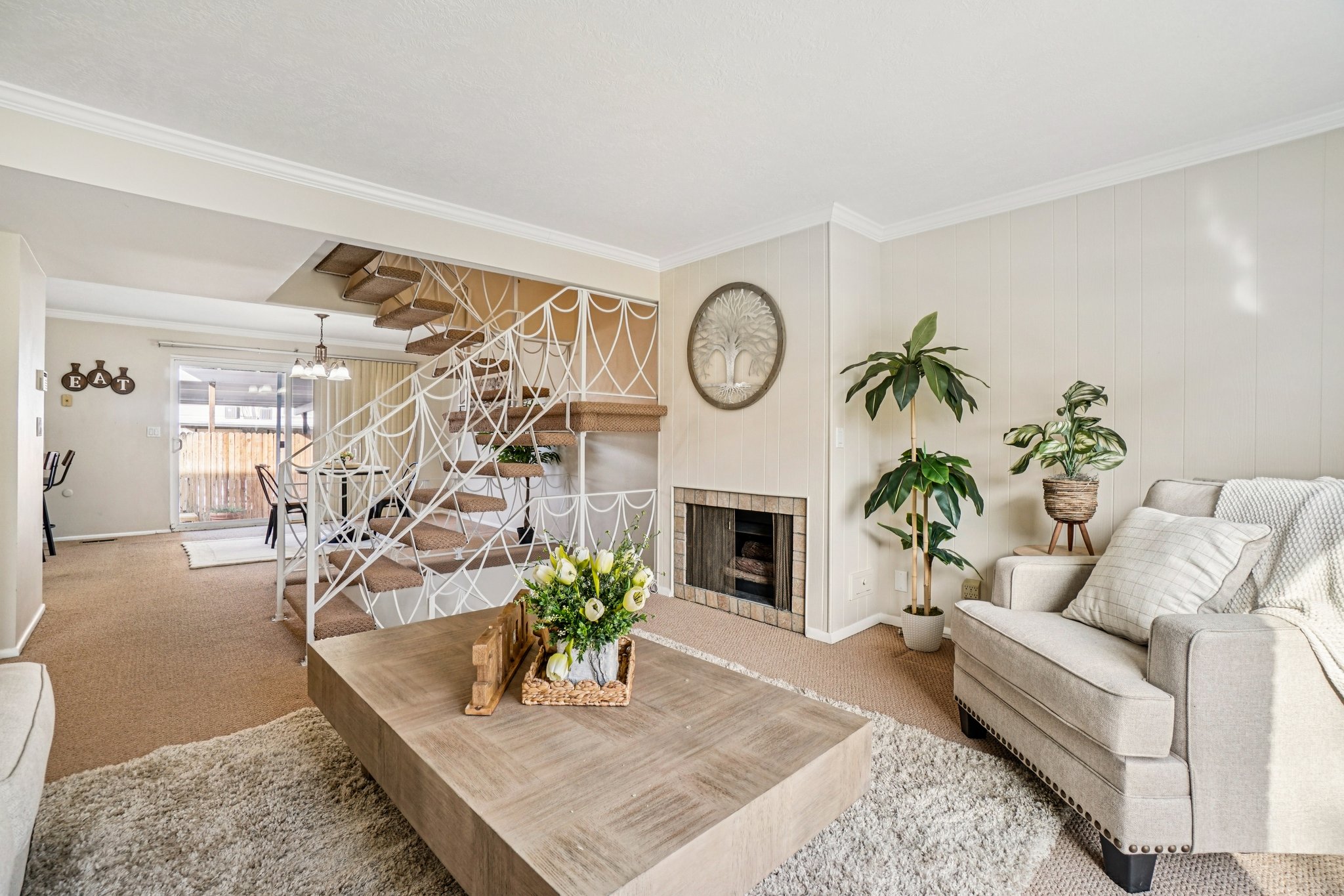 Open concept living area featuring a prominent staircase with decorative metal railing, a brick-surround fireplace, and light-toned wall paneling