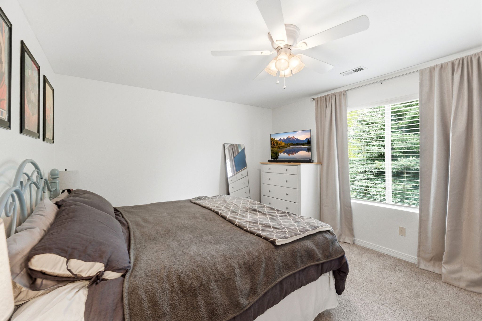 Carpeted bedroom featuring a ceiling fan, a window with horizontal blinds, and neutral-toned curtains