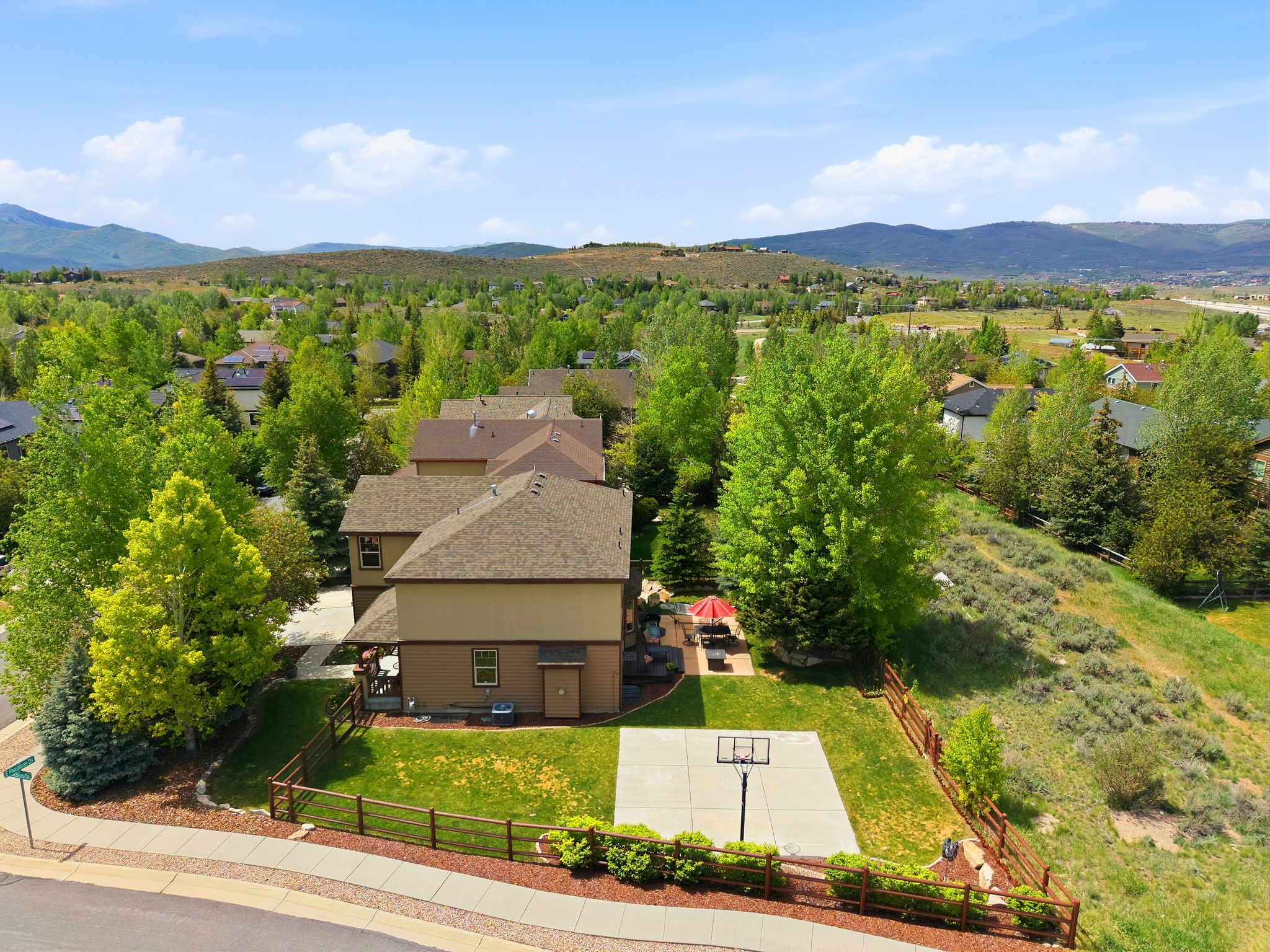 Expansive backyard featuring a concrete sport court, green lawn, and wood fencing
