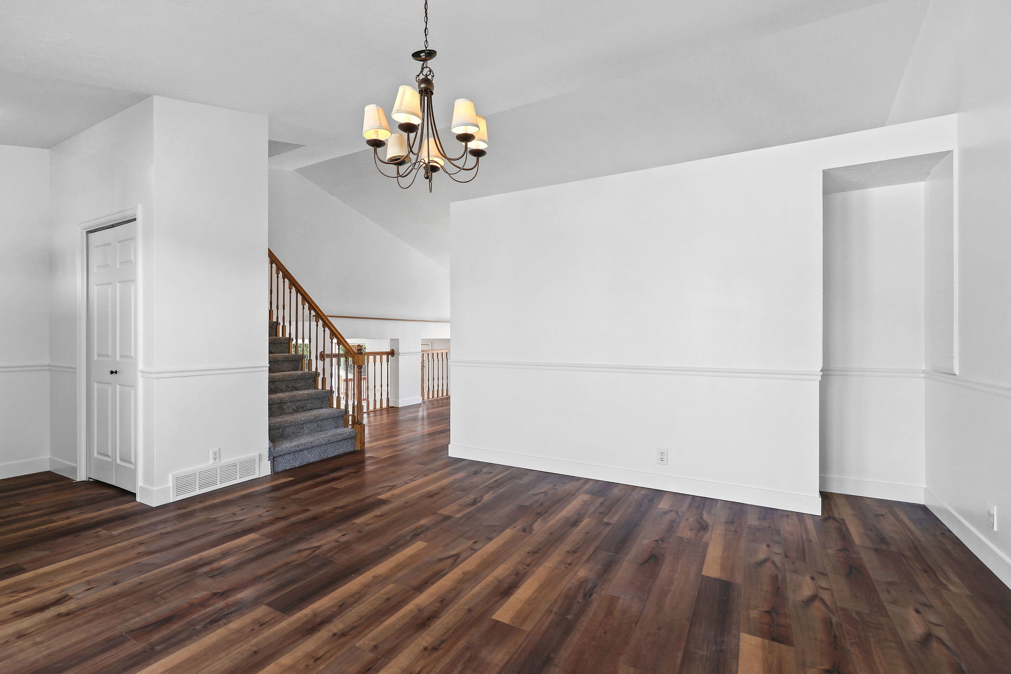 Expansive room featuring rich wood-finish flooring, crisp white wainscoting, and a detailed chandelier