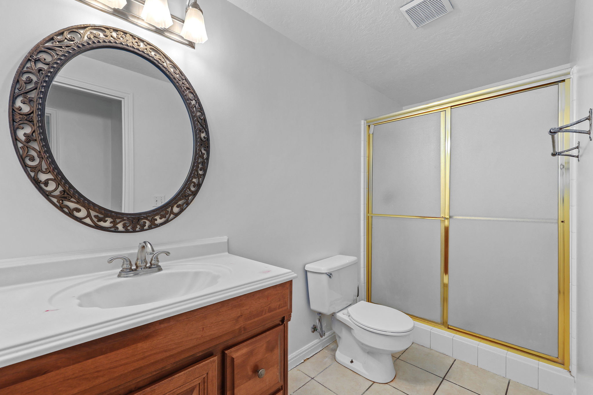 Bathroom featuring a wood-finish vanity with an integrated sink, a large oval mirror with an ornate frame, and a shower enclosure with gold-finish framing and frosted glass panels
