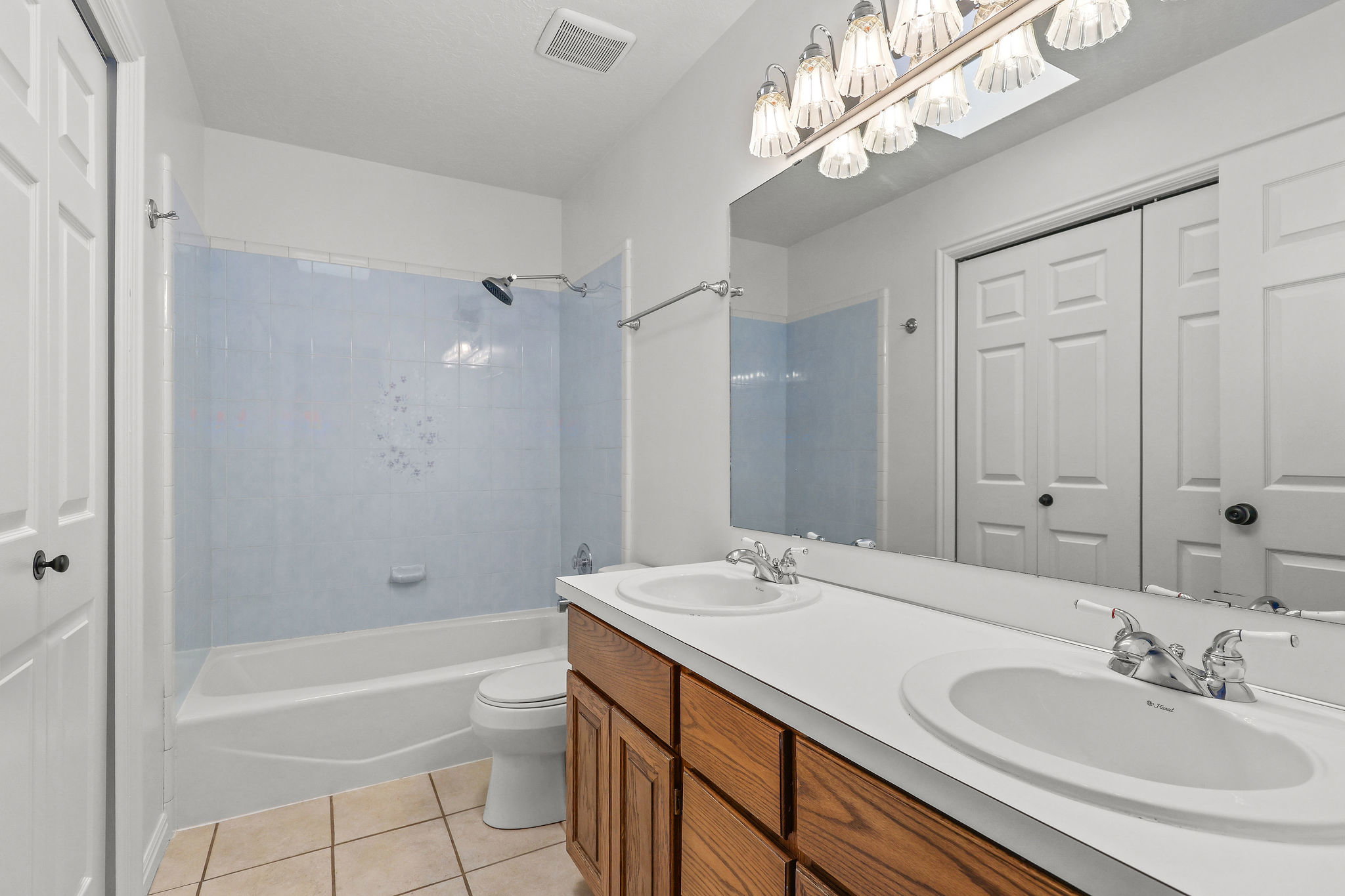 Bathroom featuring a dual vanity with wood-finish cabinetry, a large mirror, and a combined tub and shower with light blue tile surround