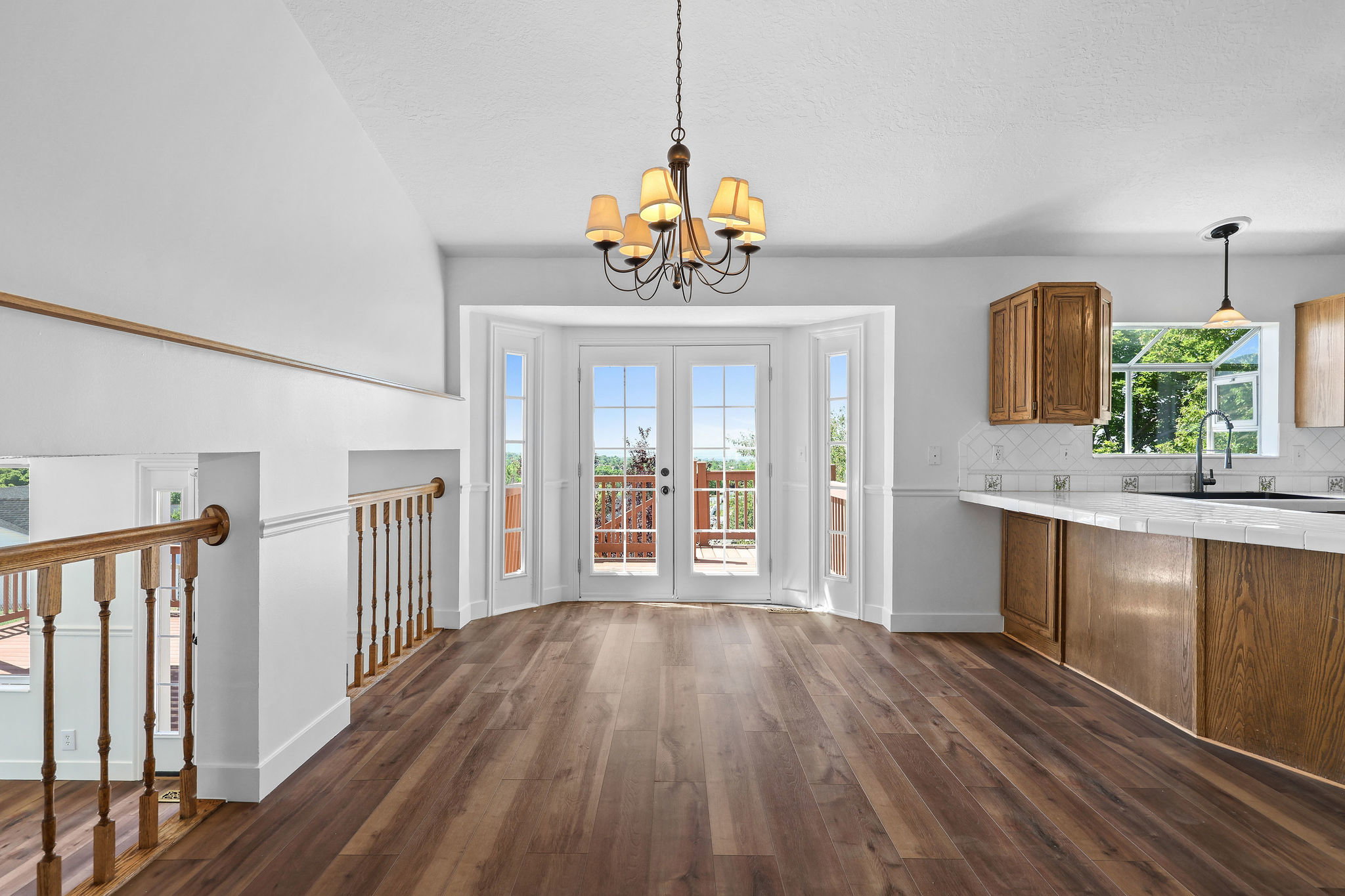 Spacious interior featuring wood-finish flooring, a contemporary chandelier, and white French doors opening to an exterior deck