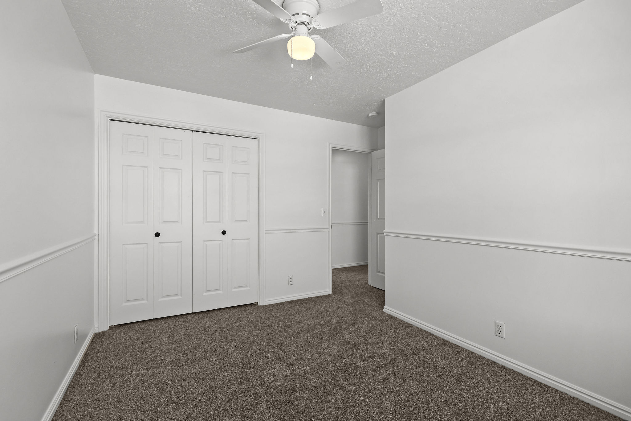 Carpeted room featuring a ceiling fan with integrated lighting, white bi-fold closet doors, and chair rail molding