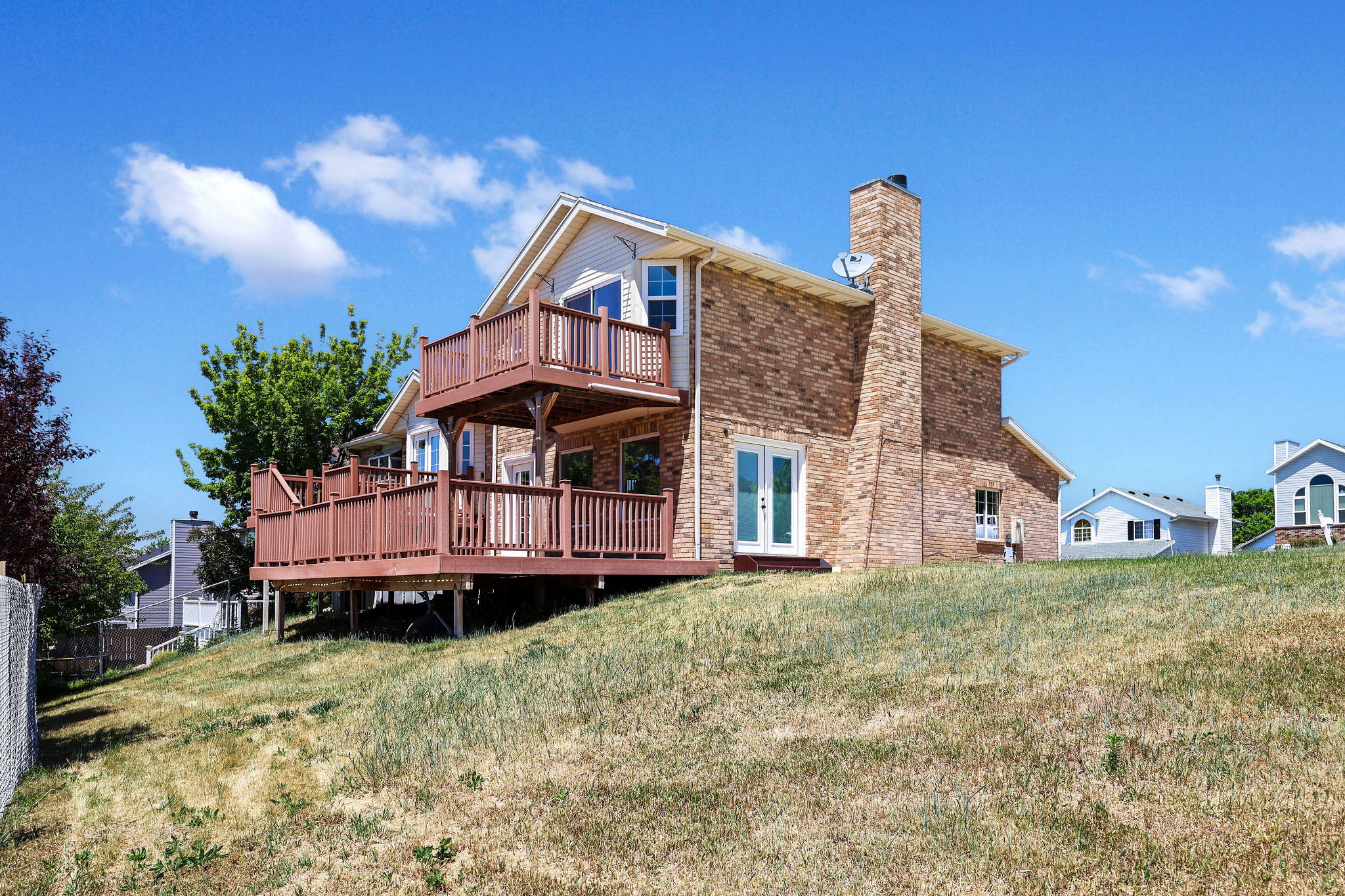Brick and siding exterior featuring a two-story deck with wood railings, a prominent brick chimney, and double French doors providing patio access