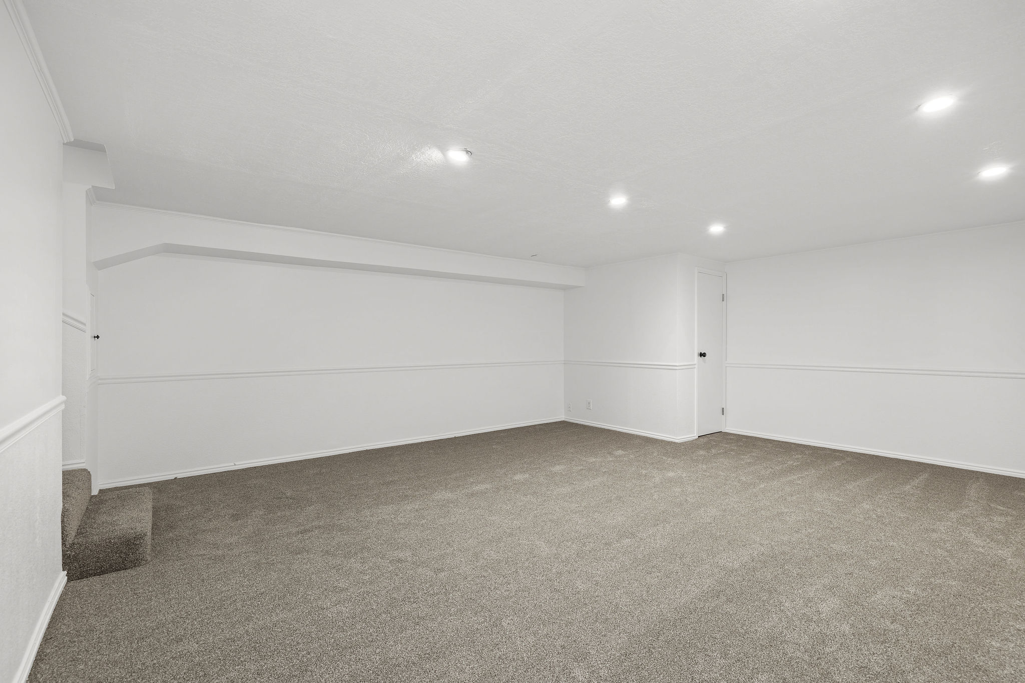 Expansive finished room featuring neutral carpeting, recessed ceiling lighting, crisp white walls, and wainscoting