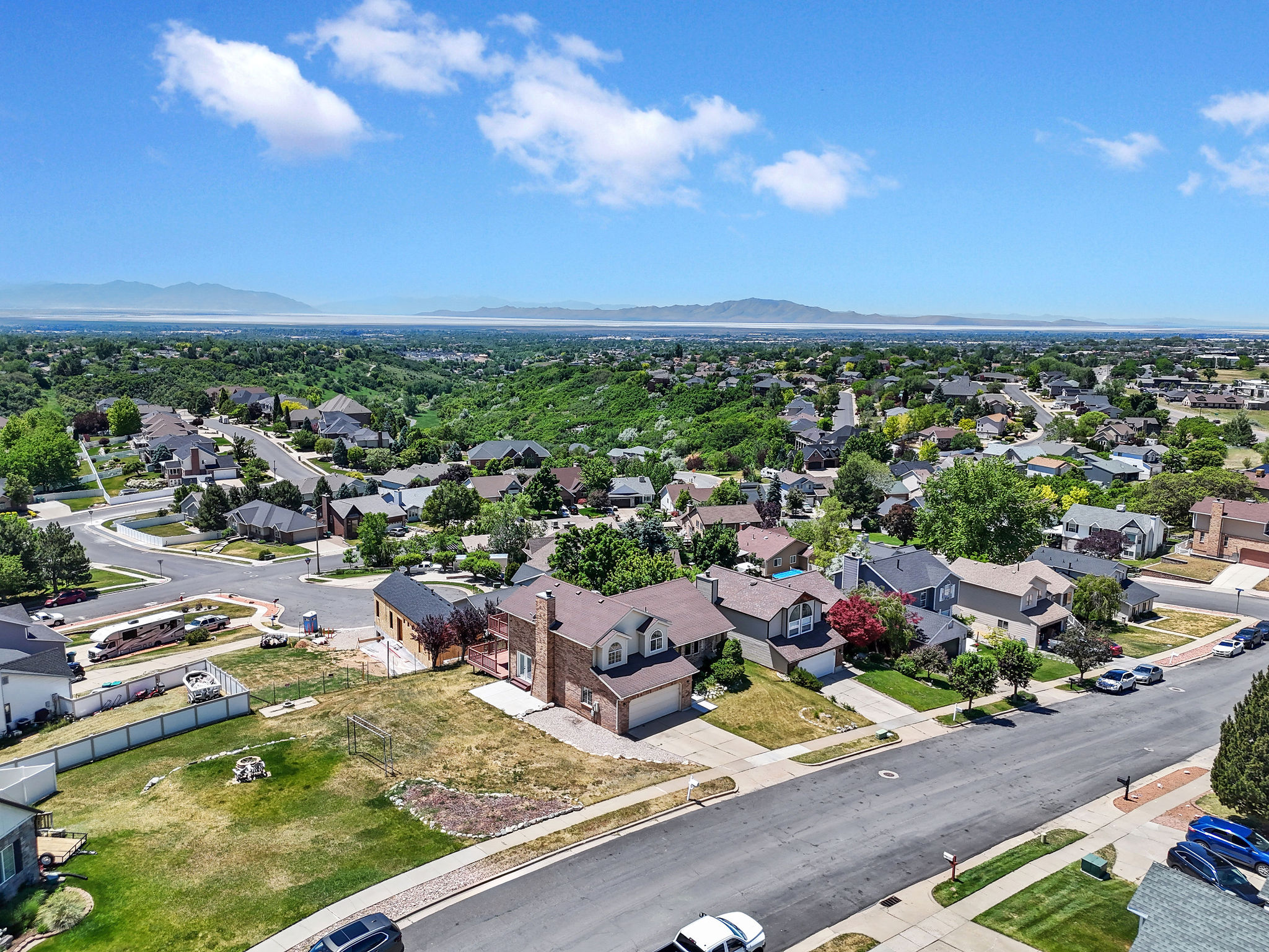 Expansive property featuring a large undeveloped lot, brick exterior home with a two-car garage, established neighborhood streets, and distant mountain ranges