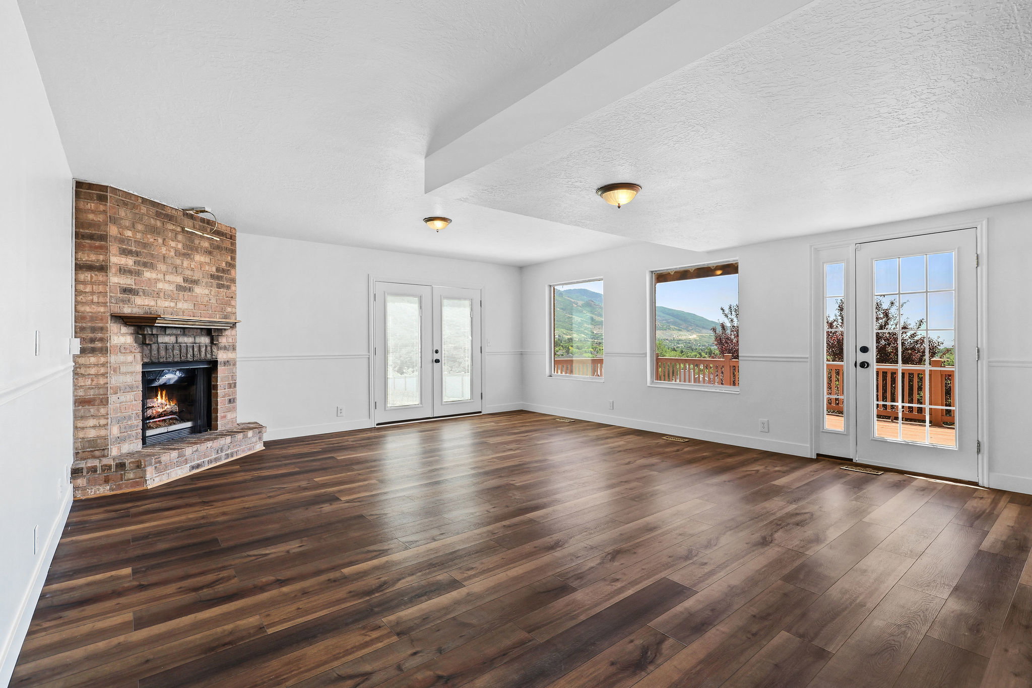 Spacious room featuring wood-finish flooring, a brick fireplace with a mantel, and white wainscoting