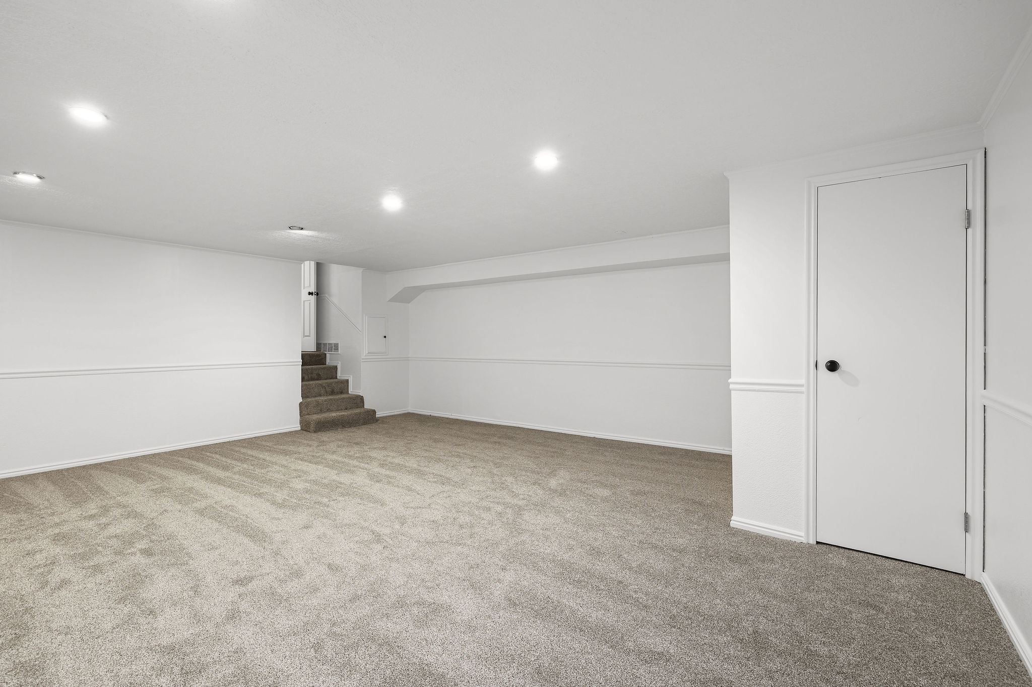 Spacious carpeted room featuring recessed lighting, white walls with wainscoting, and a white interior door