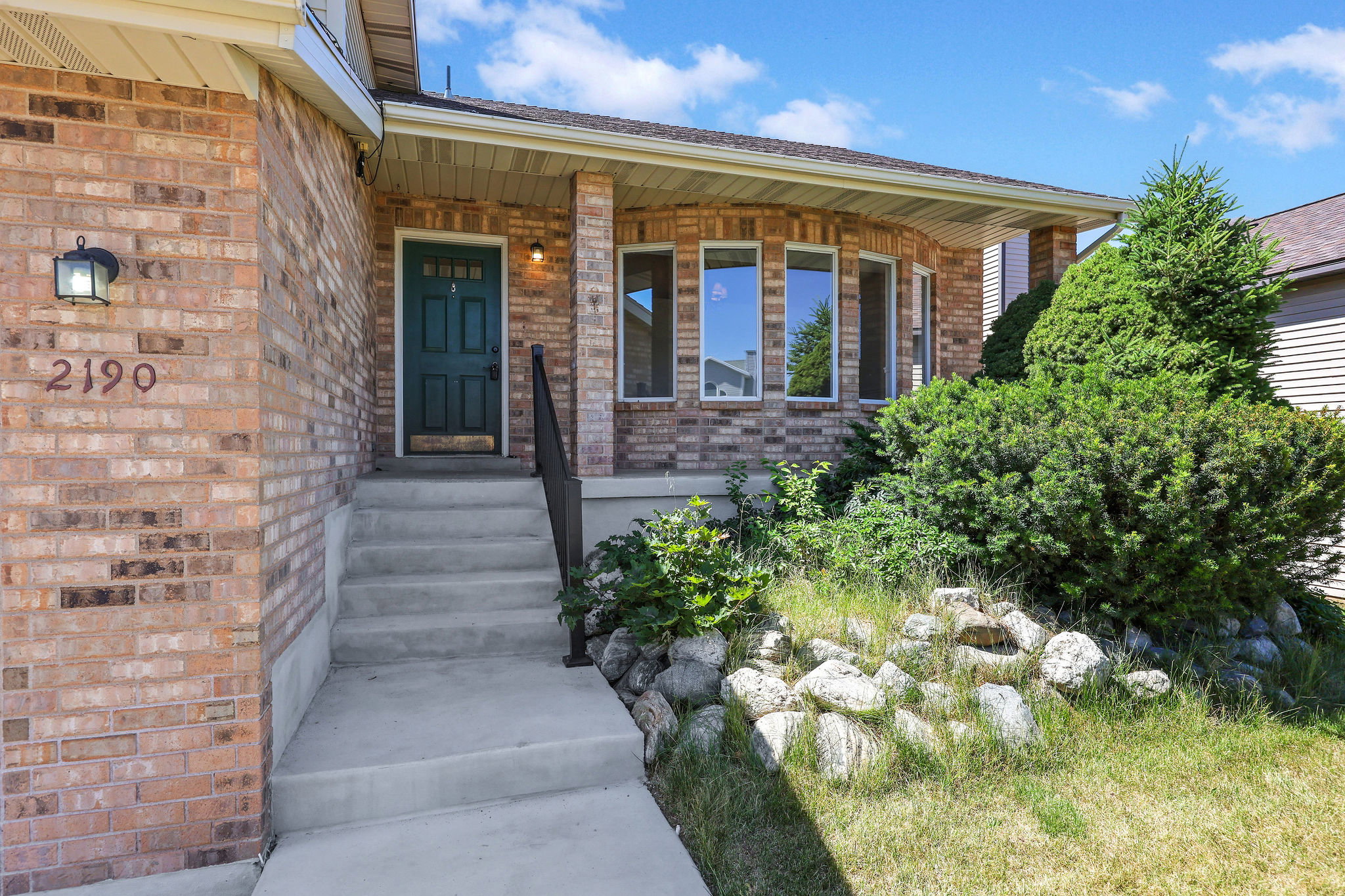 Brick facade residence featuring a covered front porch, dark paneled entry door, and a bay window