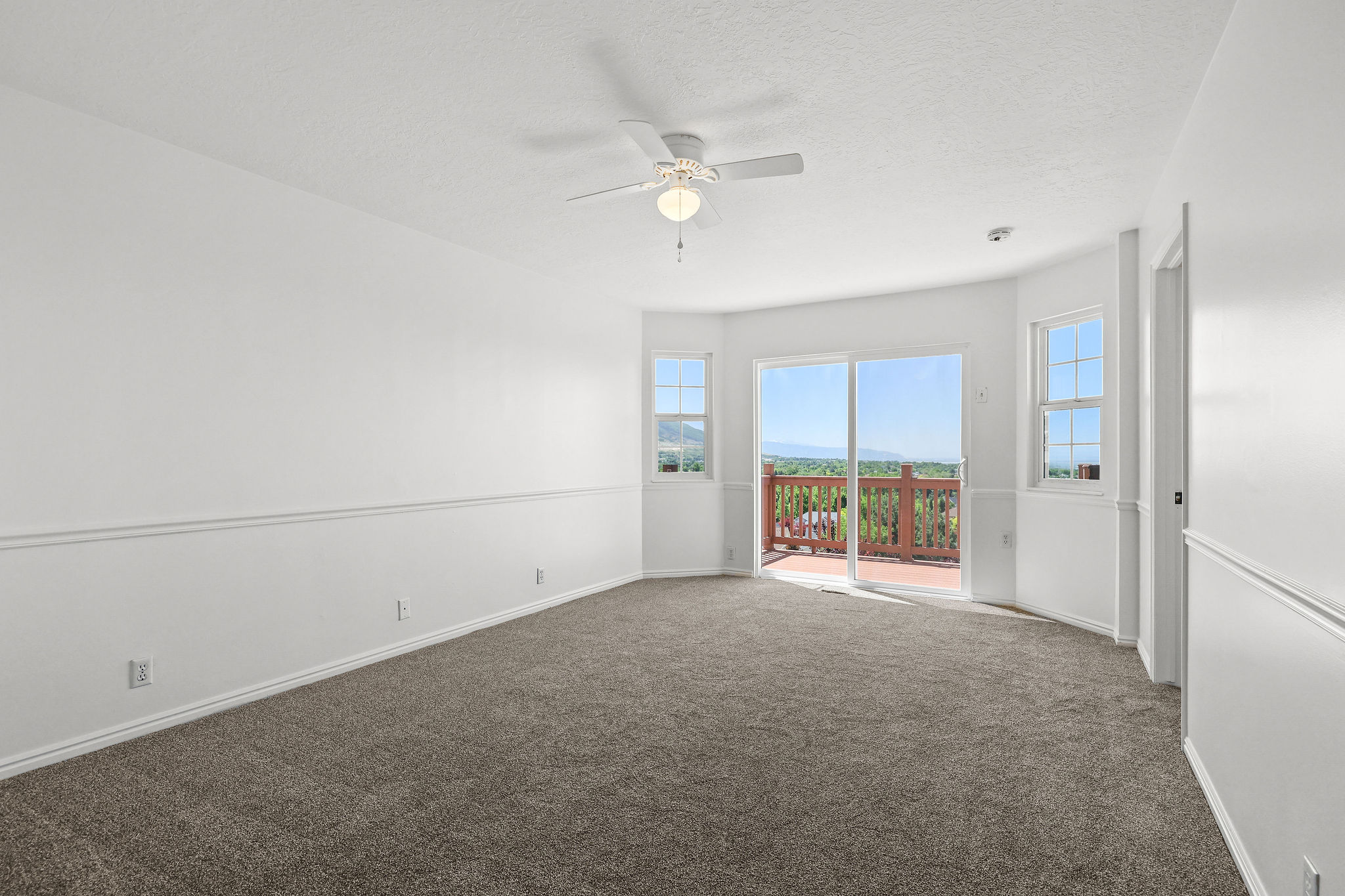 Carpeted room with a ceiling fan and a curved wall featuring a sliding glass door and two windows