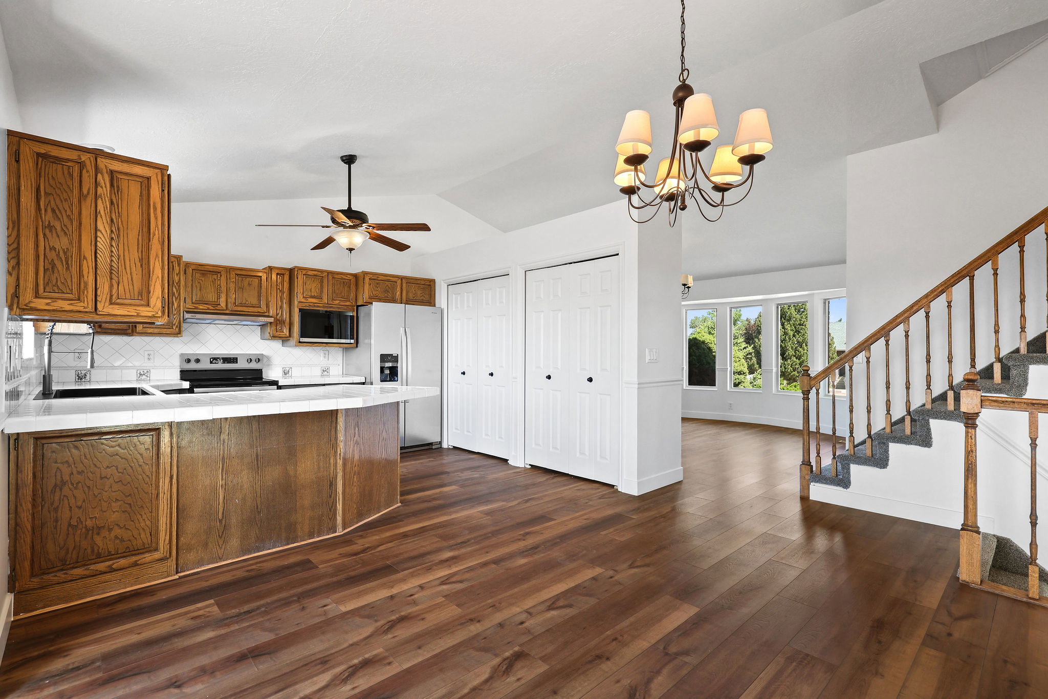 Open-concept kitchen featuring wood cabinetry, white countertops, tile backsplash, and stainless steel appliances