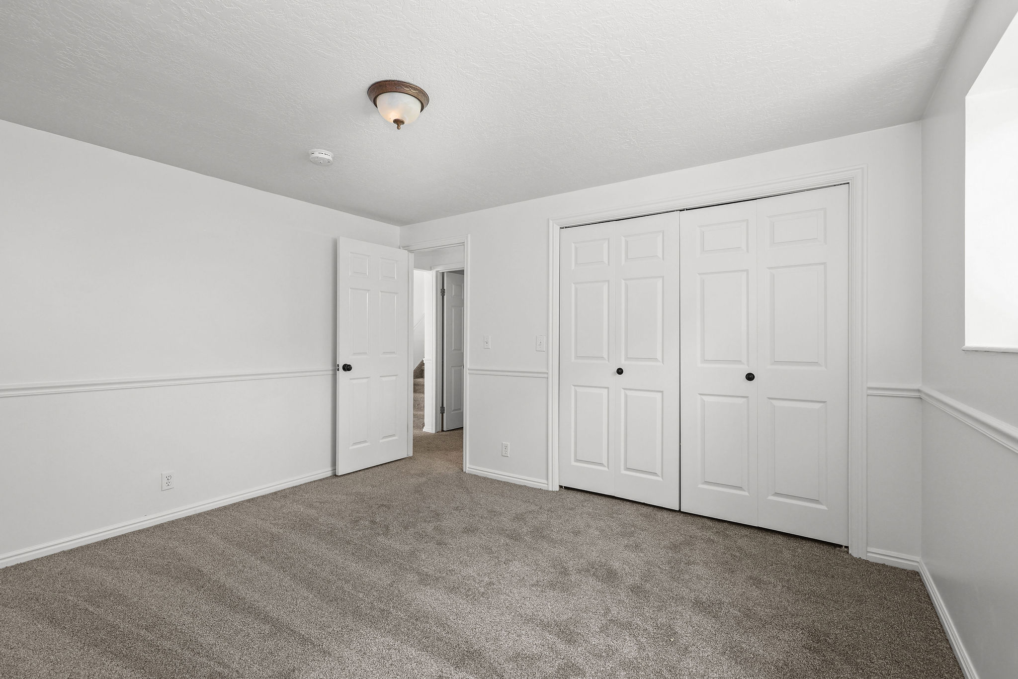 Carpeted room featuring white walls, wainscoting, a ceiling-mounted light fixture, and double bi-fold closet doors