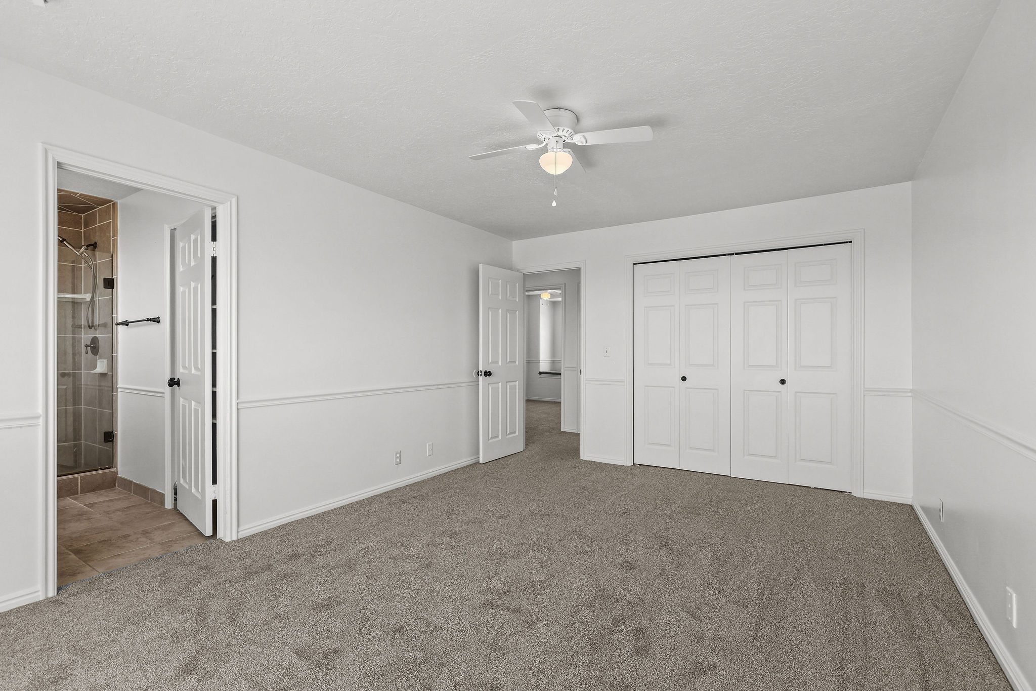 Spacious room featuring neutral carpeting, white walls with wainscoting, and a ceiling fan