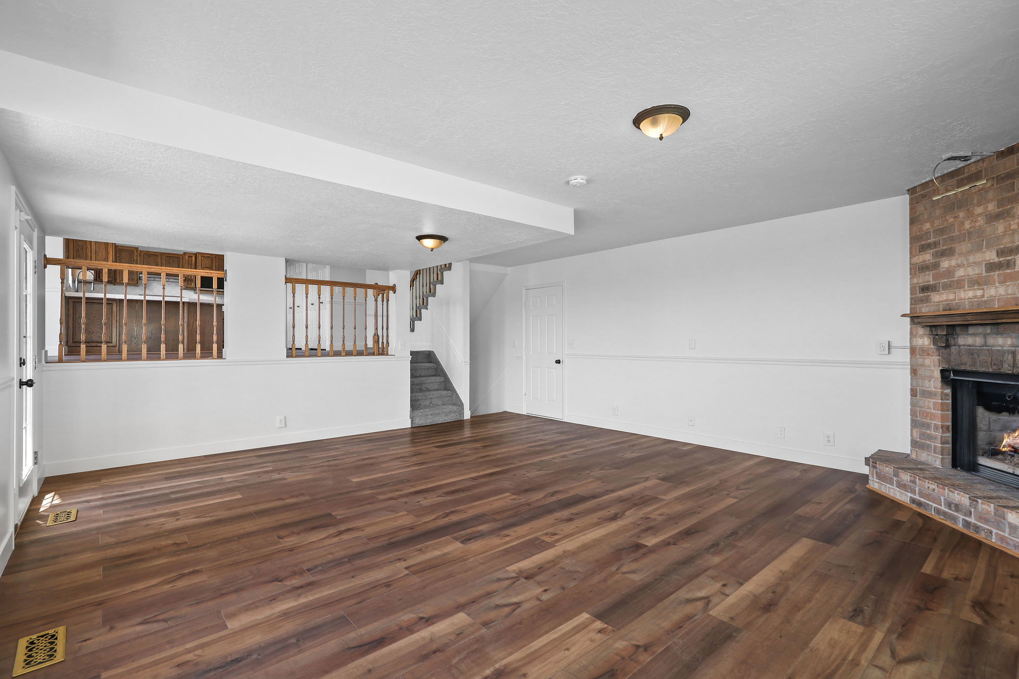Spacious room featuring wood-finish flooring, a brick fireplace with a hearth, and a built-in wooden railing