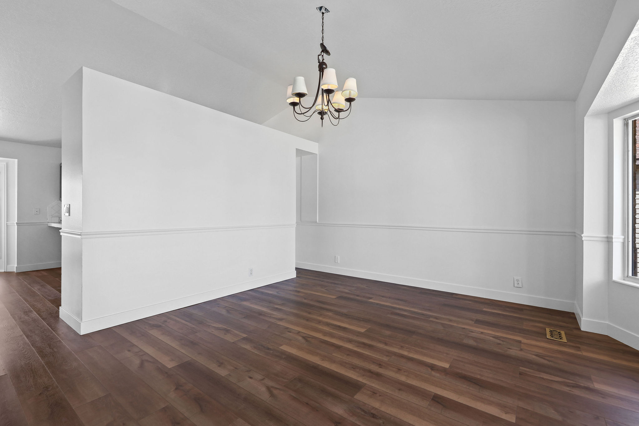 Spacious room featuring wood-finish flooring, white walls with wainscoting, and a bay window
