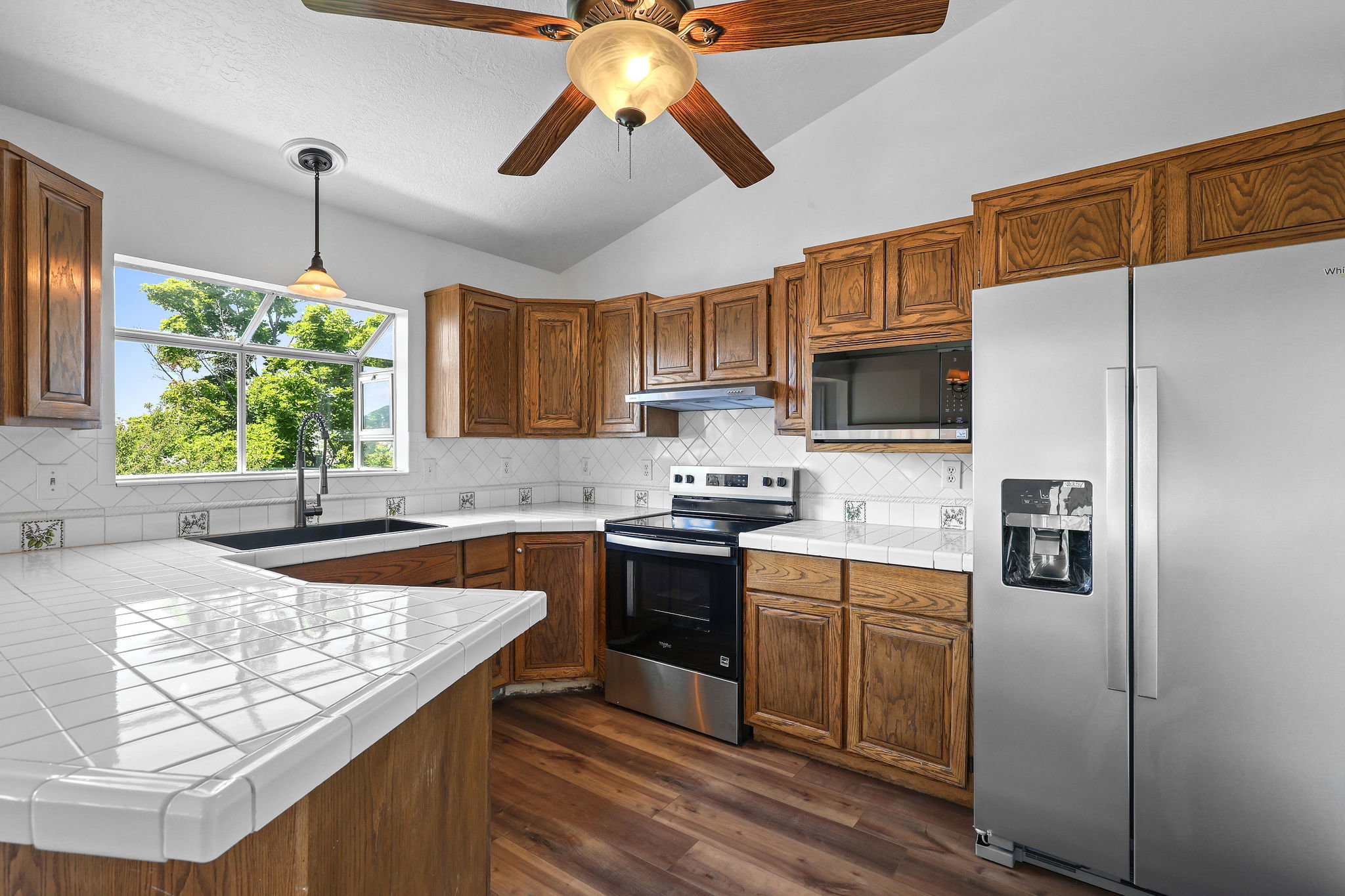 Kitchen featuring wood-finish cabinetry, stainless steel appliances, white tile countertops, and a full tile backsplash