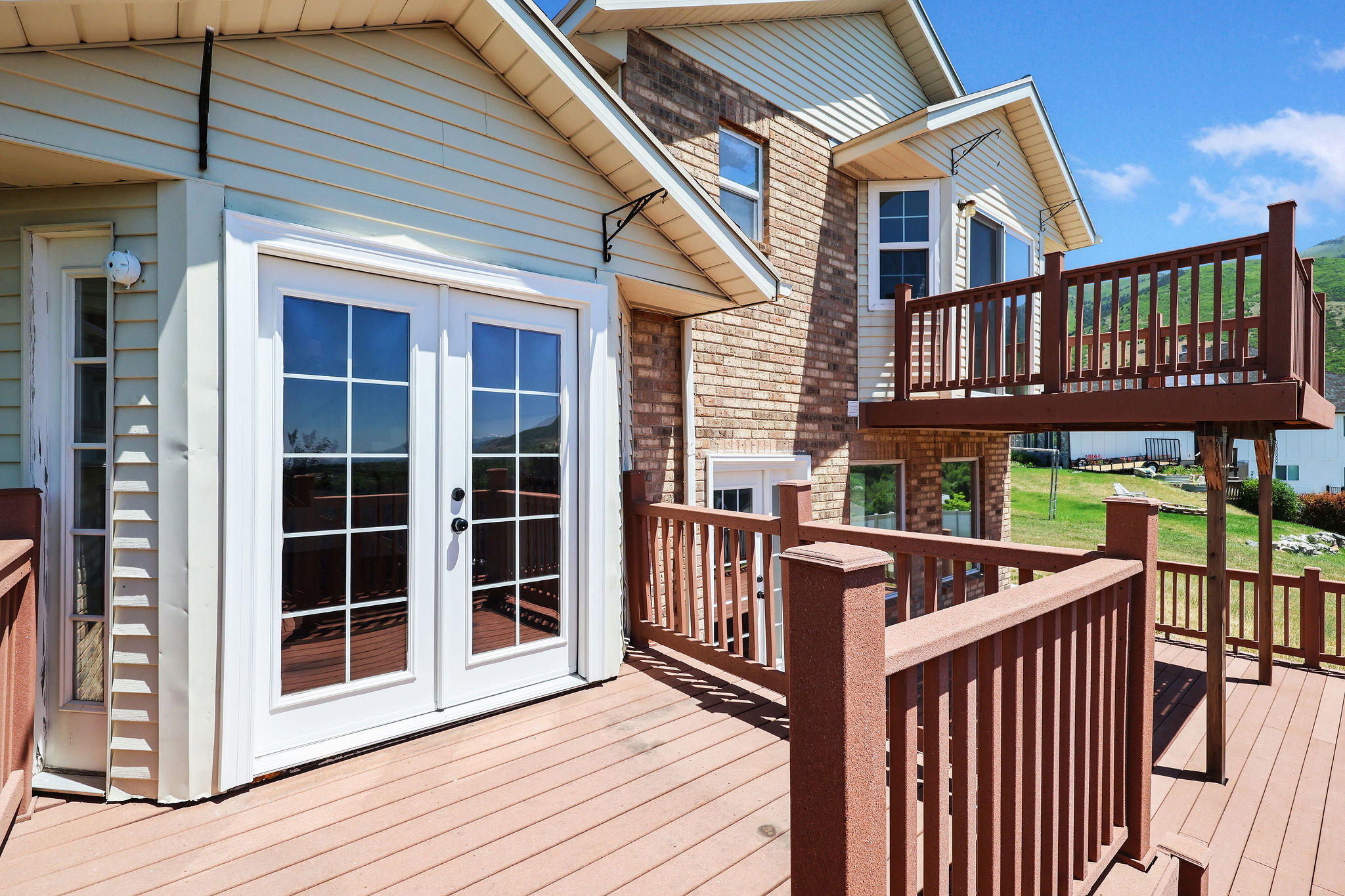 Expansive multi-level wood-finish deck featuring full railings, a set of white French doors, and an additional single-panel glass door