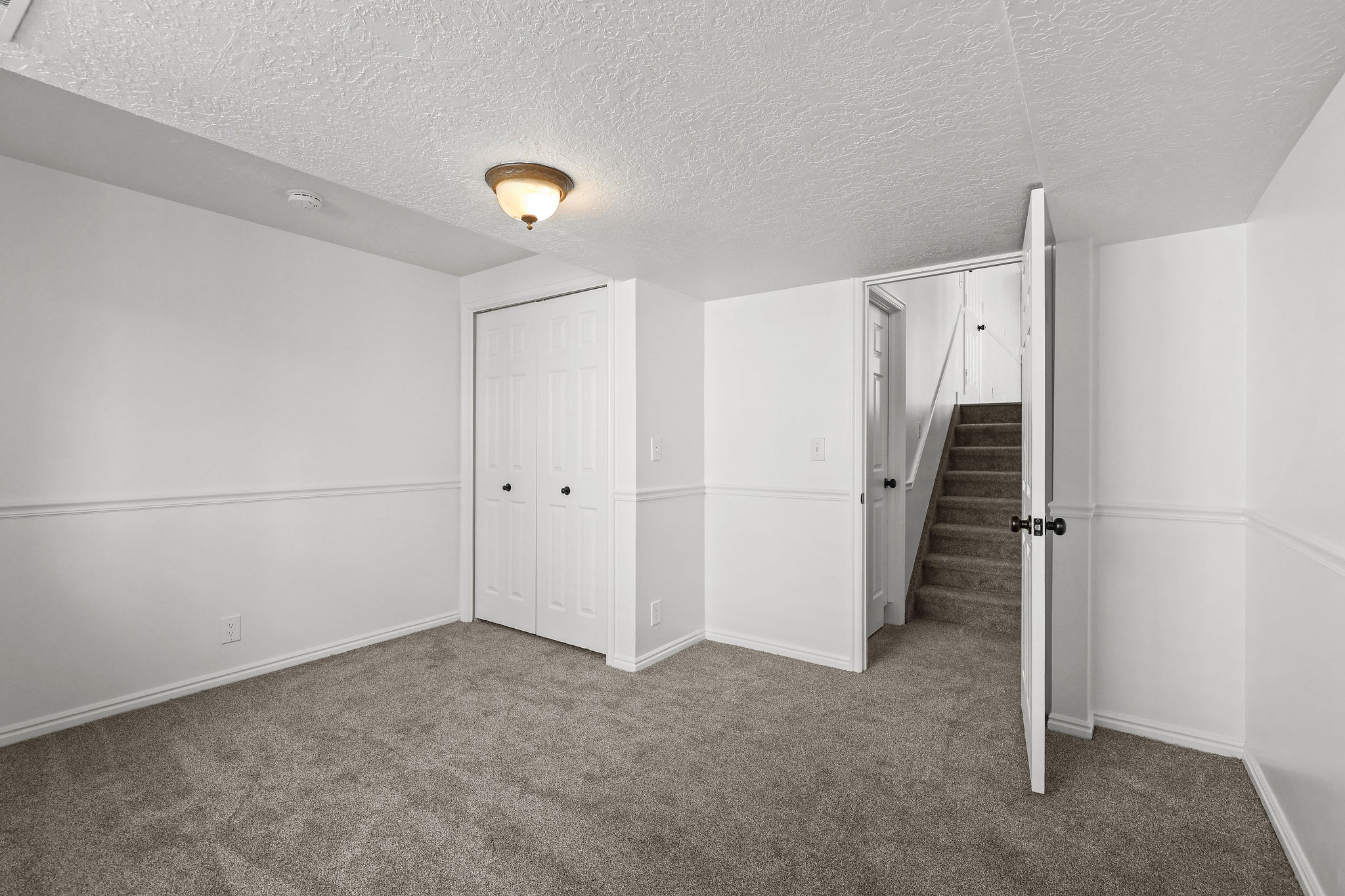 Carpeted room featuring white walls with chair rail molding, a flush mount ceiling light, and a bi-fold closet door with black hardware