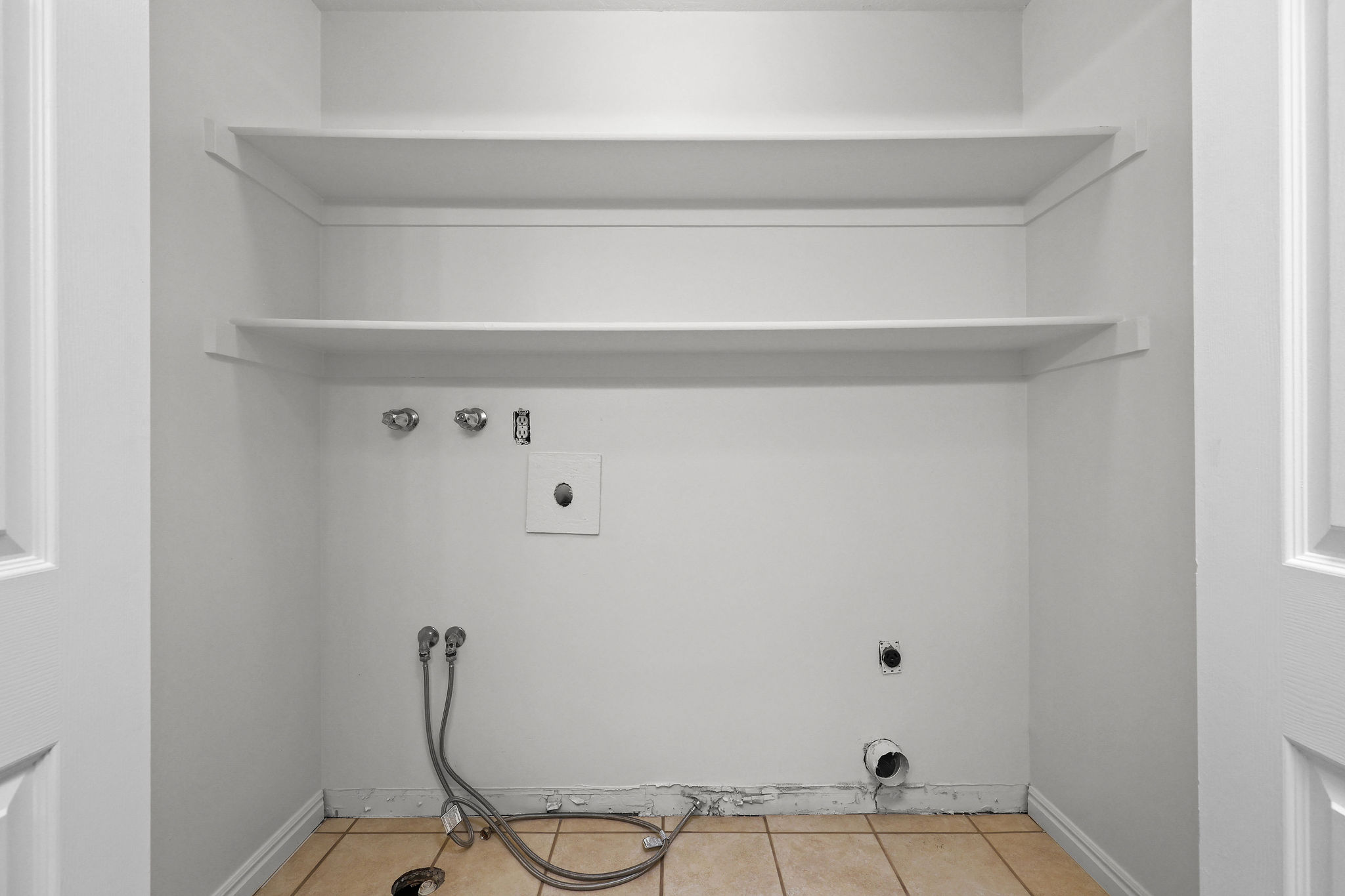 Dedicated laundry area featuring ceramic tile flooring, two white shelving units, and plumbing connections