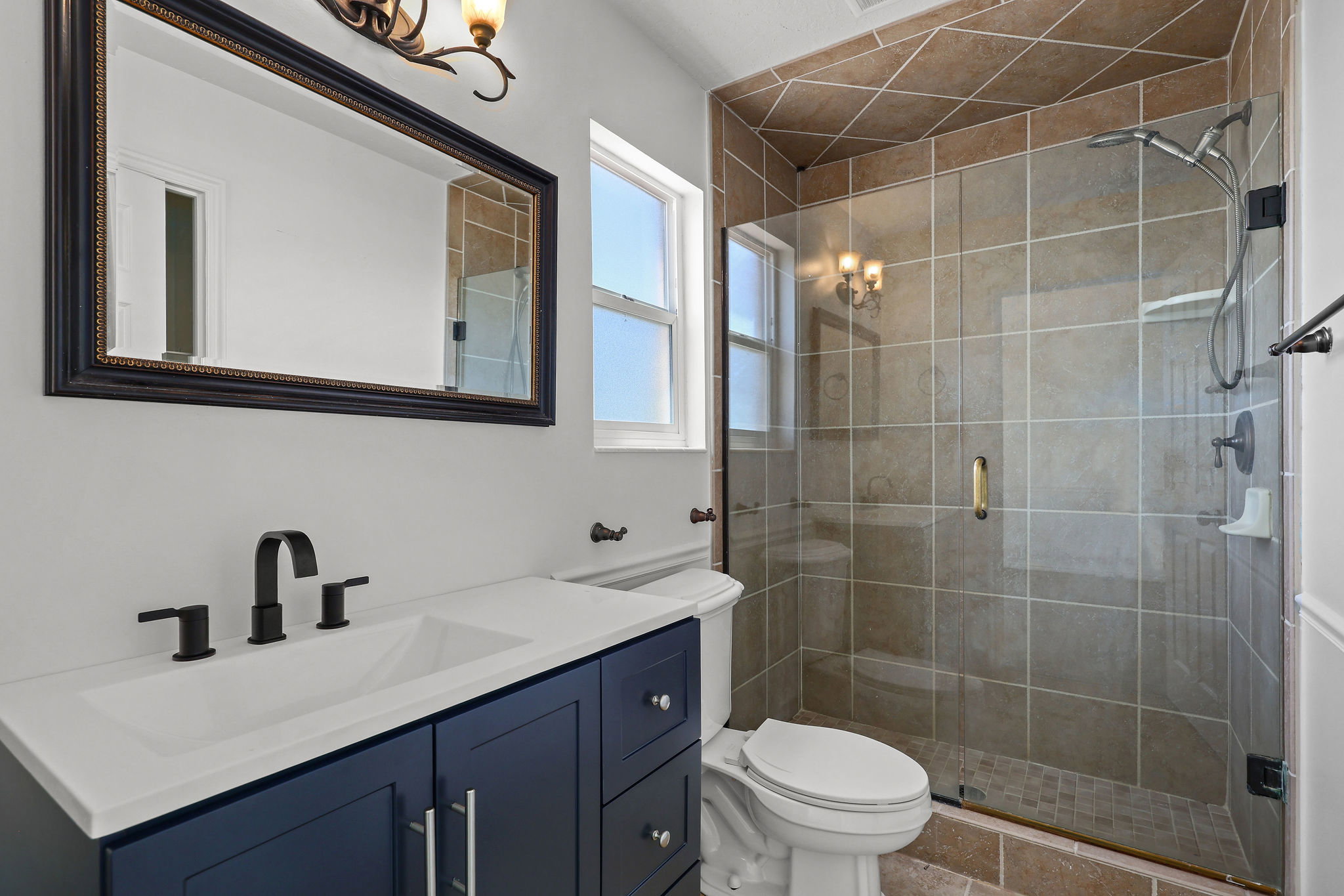Bathroom featuring a dark blue vanity with a white countertop, matte black faucet, and a large framed mirror