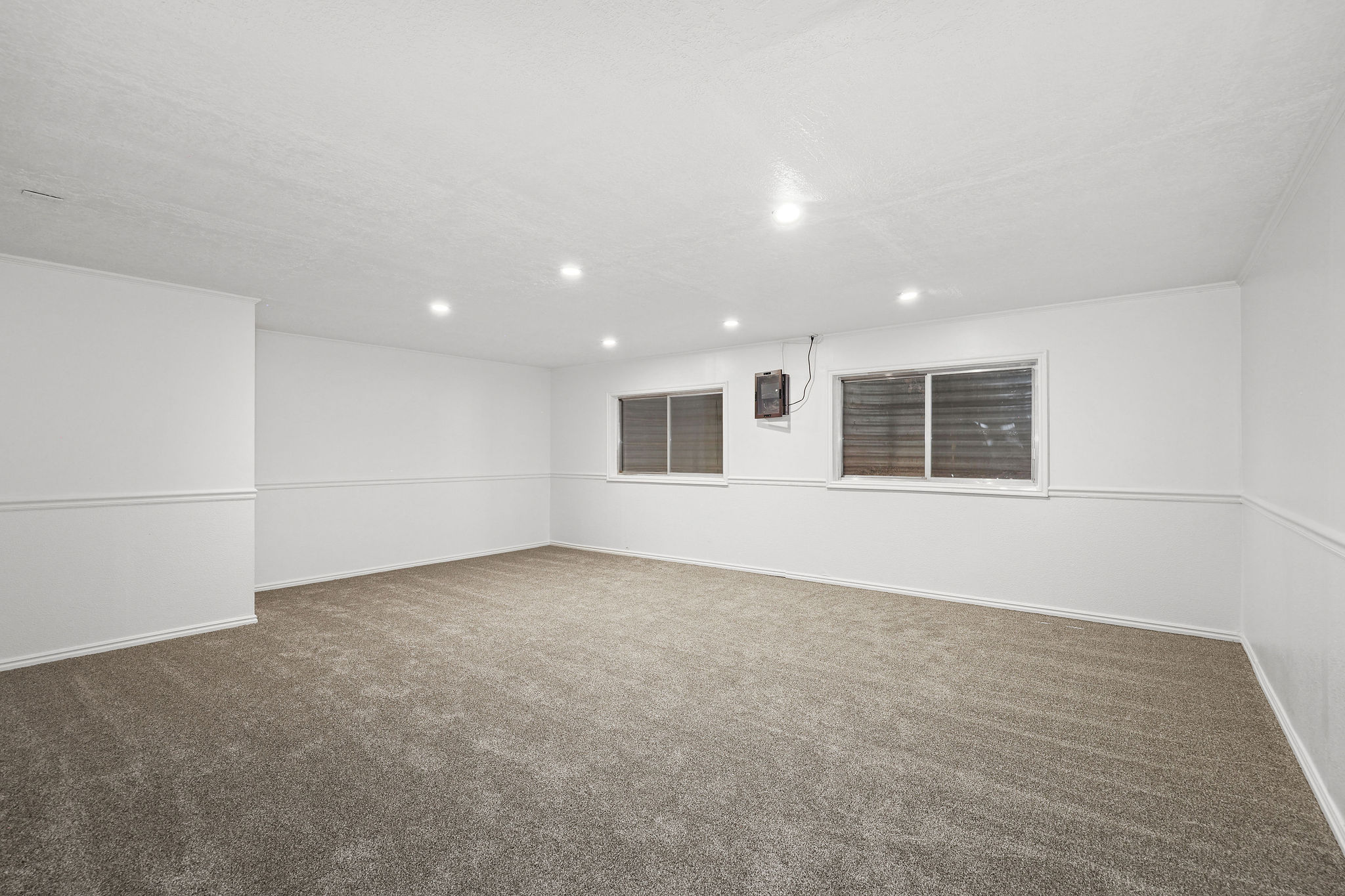 Spacious room featuring plush carpet flooring, recessed lighting, white walls with chair rail molding, and two windows