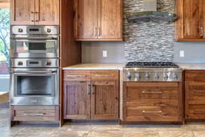 Stainless steel range with a mosaic tile backsplash and overhead hood