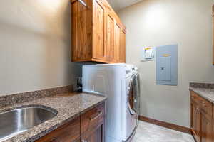 Utility area featuring rich wood cabinetry, granite-finish countertops, stainless steel sink, and durable tile flooring