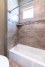 Bathtub and shower combination featuring neutral-toned tile surround, decorative mosaic tile accent band, built-in shower niche, and a privacy window