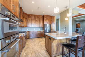 Kitchen featuring extensive wood cabinetry, double wall ovens, a large center island with a curved countertop, stainless steel appliances, and recessed lighting