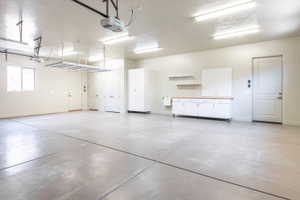 Spacious garage featuring concrete flooring, overhead storage racks, built-in white cabinetry with a wood-finish countertop, and multiple overhead fluorescent light fixtures