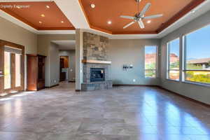 Spacious living area featuring large format tile flooring, a stone fireplace with a wood mantle, a tray ceiling with recessed lighting and a ceiling fan, and multiple large windows