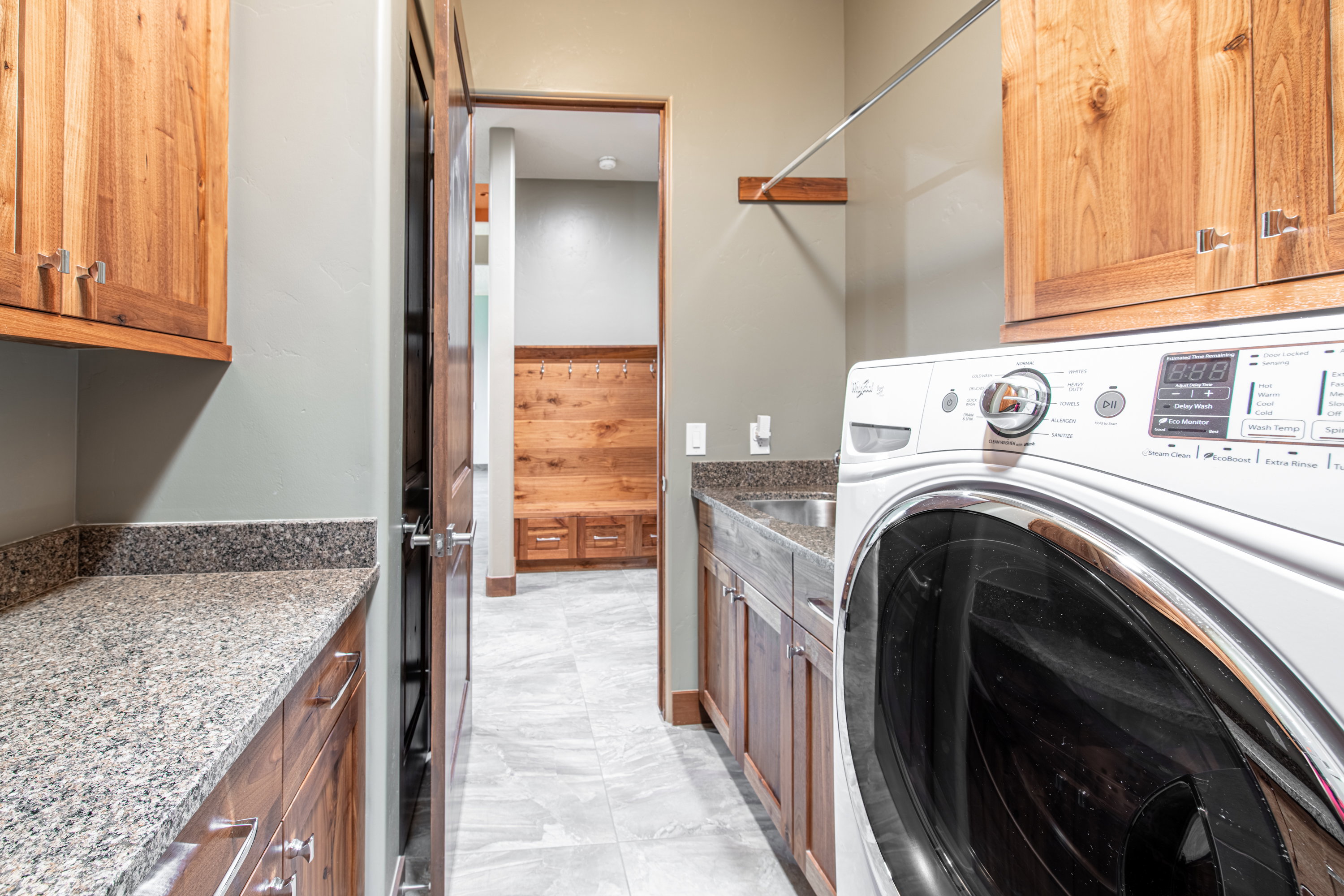 Laundry area featuring wood cabinetry, granite-finish countertops, built-in sink, and tile flooring