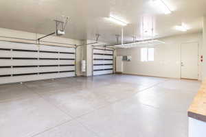 Spacious garage featuring two sectional garage doors with automatic openers, an epoxy-coated concrete floor, ample overhead lighting, and built-in overhead storage racks