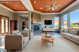 Spacious living area featuring a stone-clad fireplace with a wood mantel, high tray ceilings, recessed lighting, and large windows