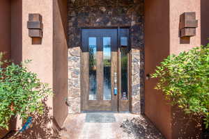 Entryway featuring a wood-panel door with vertical glass inserts, stone veneer detailing, stucco exterior, and modern wall sconces