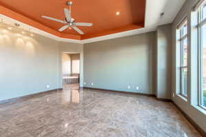 Spacious interior room featuring polished tile flooring, a tiered ceiling with an orange accent, and a ceiling fan