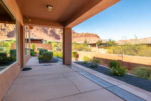 Spacious covered patio featuring concrete flooring with decorative inlay, stucco exterior, built-in recessed lighting, and low-maintenance landscaping with dark aggregate