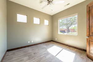 Spacious room featuring wood-finish flooring, a ceiling fan, and multiple windows for natural illumination