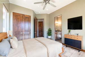 Bedroom featuring a ceiling fan, light wood-finish flooring, wood double doors, and an entry to a bathroom with a double vanity