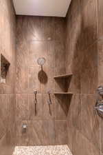 Shower with large format brown-toned wall tiles, a rainfall showerhead, multiple body sprays, a built-in corner shelf, and a mosaic pebble floor
