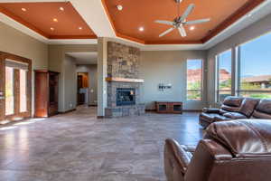 Spacious living area featuring a stone-clad fireplace with a wood mantel, coffered ceilings with recessed lighting, large windows, and tile flooring