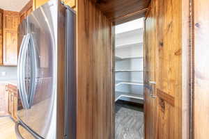 Walk-in pantry with ample shelving and grey tile flooring, featuring natural wood-finish walls and a coordinating door with brushed nickel hardware