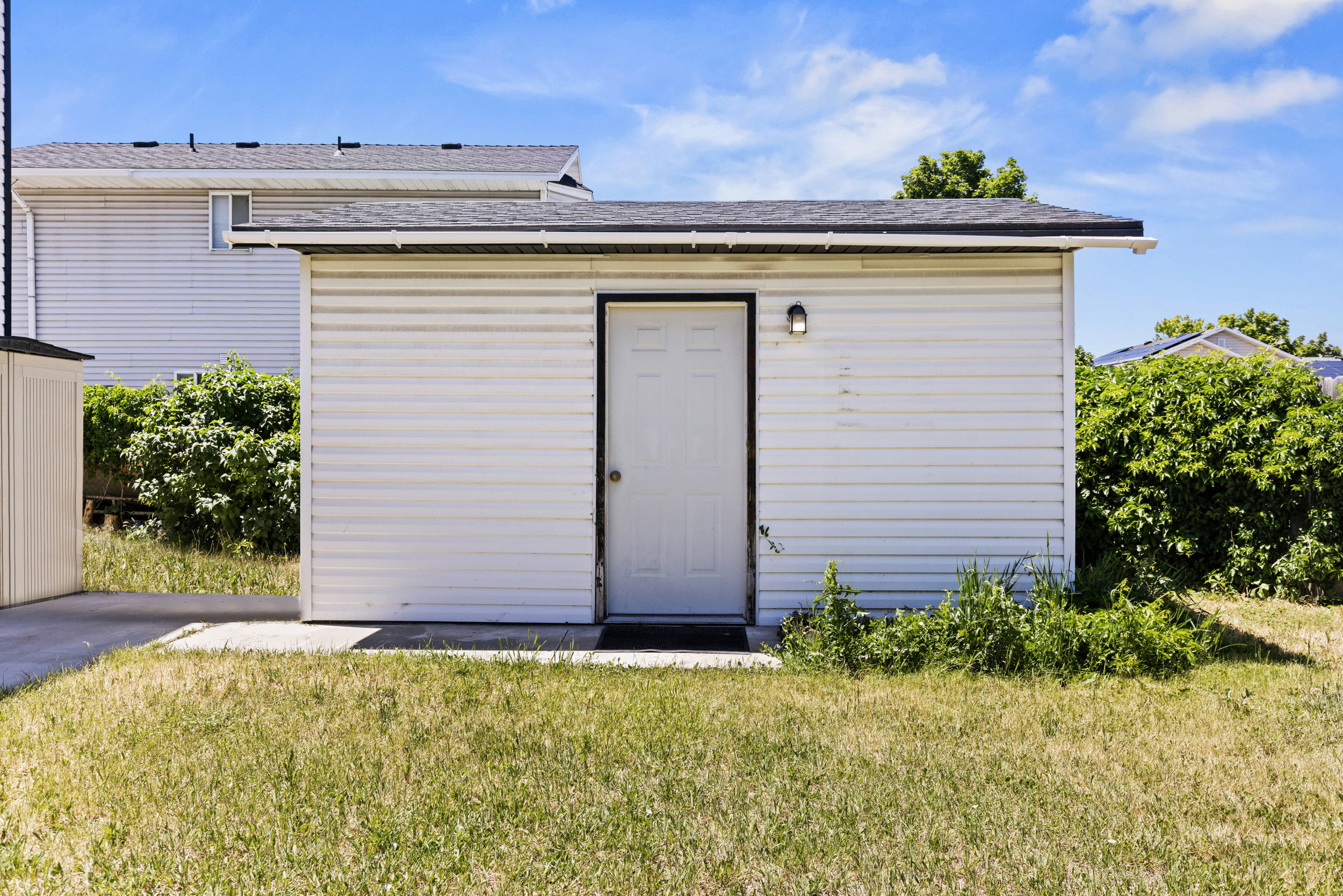 Detached auxiliary building featuring white siding, a single entry door, and exterior lighting