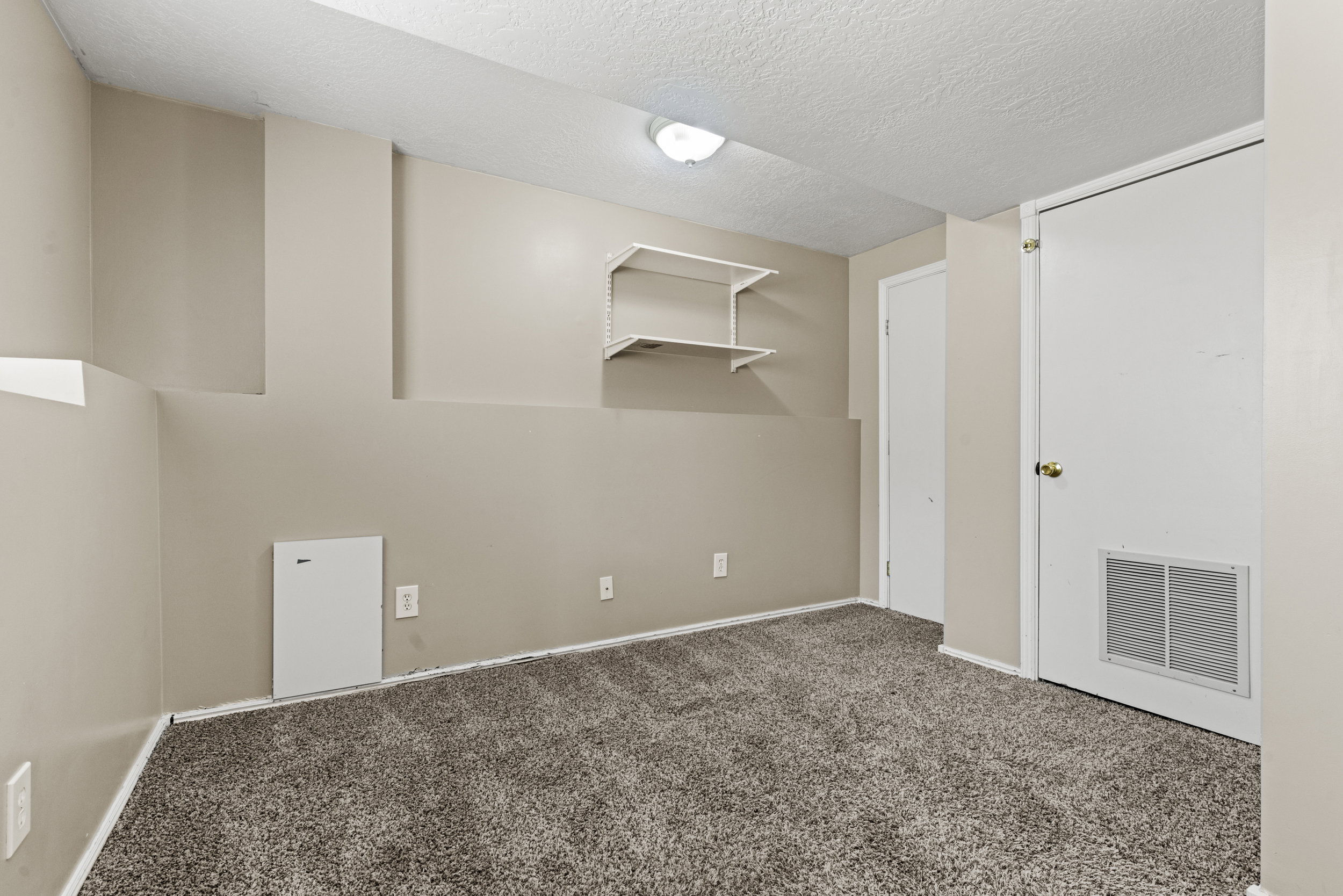 Carpeted room featuring neutral wall tones, built-in wall shelving, a flush-mount ceiling light fixture, and white trim