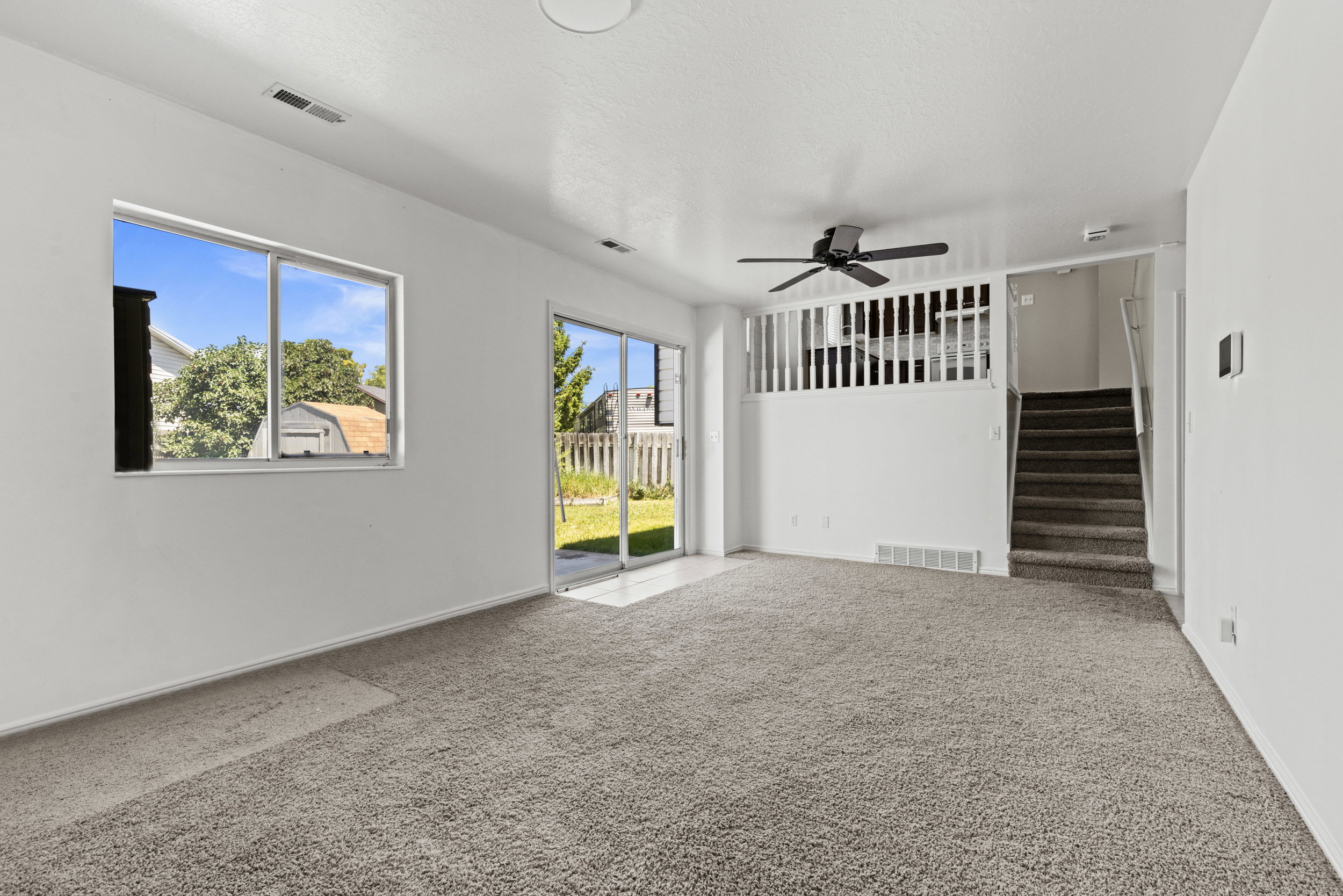 Carpeted living area featuring a ceiling fan, a large window, and a sliding glass door providing access to the exterior