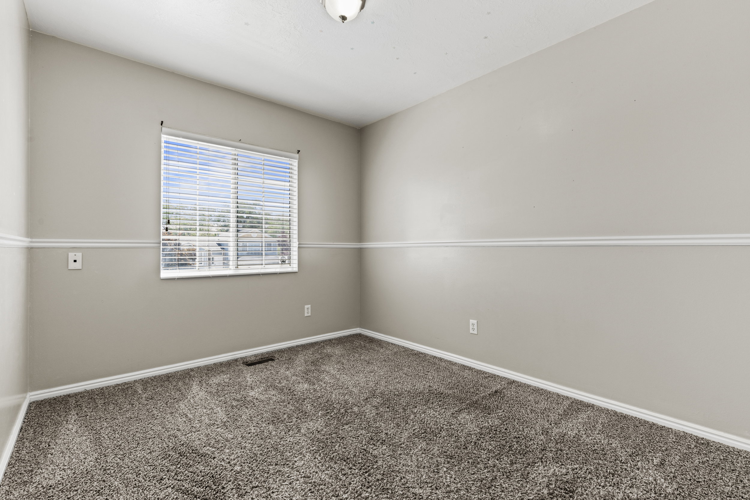 Carpeted room featuring a single window with horizontal blinds, neutral-toned walls, and a white ceiling
