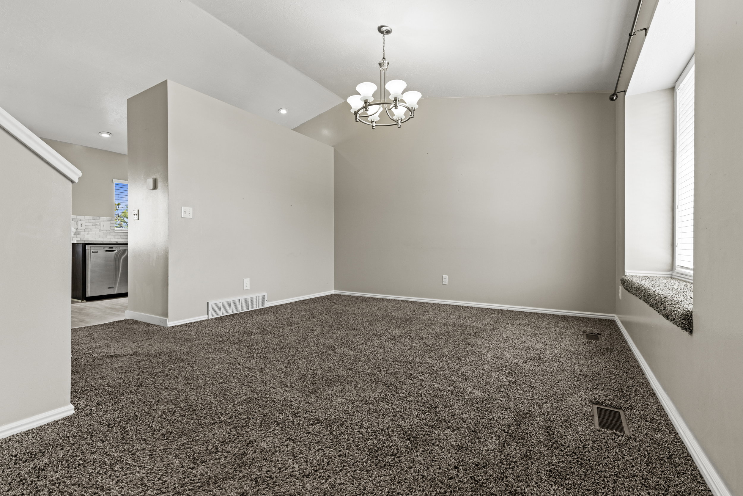 Spacious living area featuring neutral-toned carpeting, a contemporary chandelier, a window seat with blinds, and recessed lighting